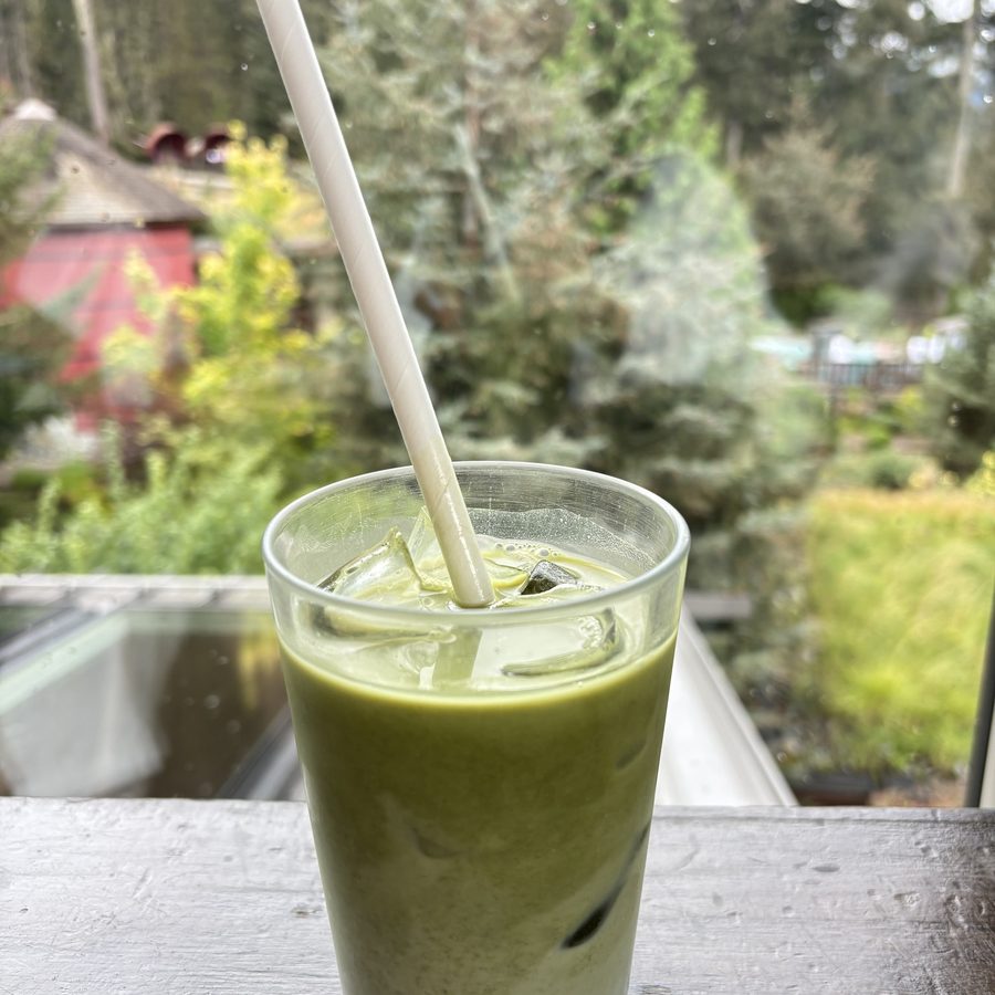 A green drink on a table beside a window and plants