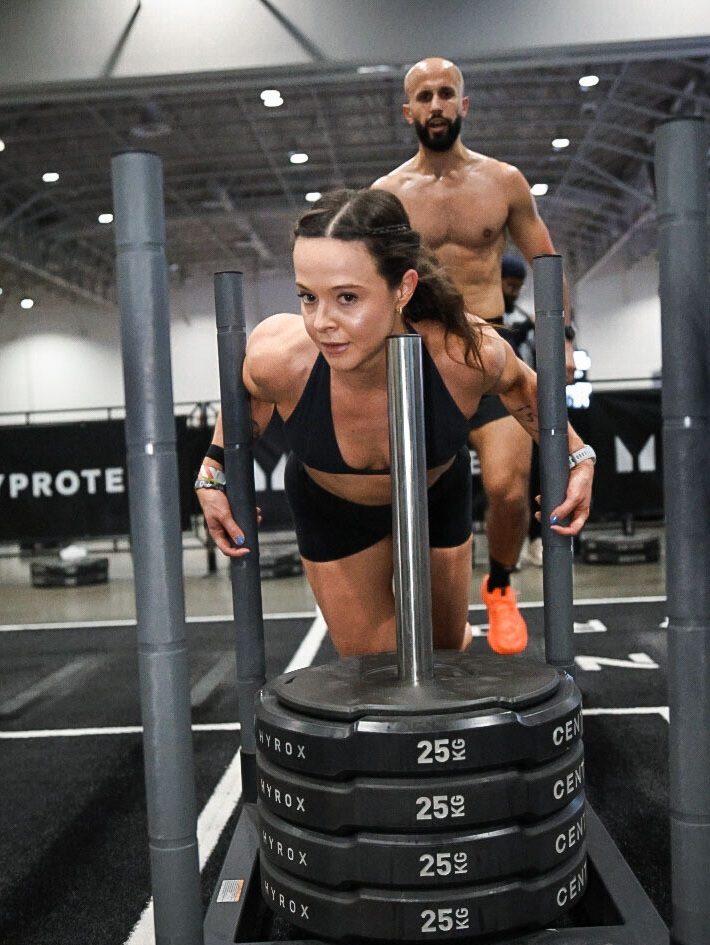 Alana pushing a weighted sled toward the camera during her HYROX race
